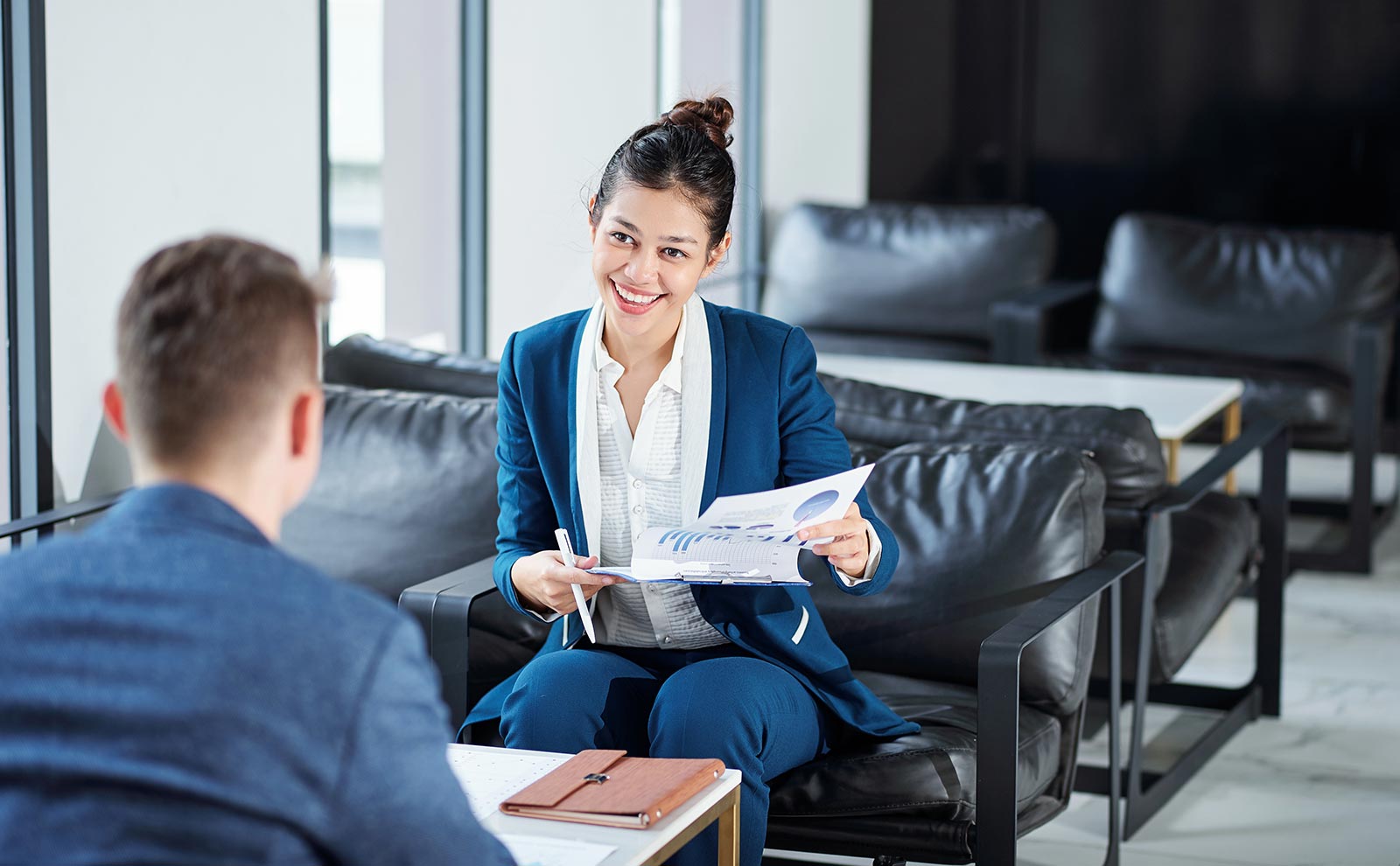 a smiling woman holding papers and looking at a man